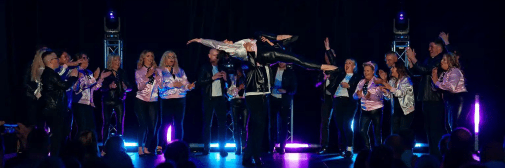 Lady being held up by a gentleman in a dance move with other dances around her clapping